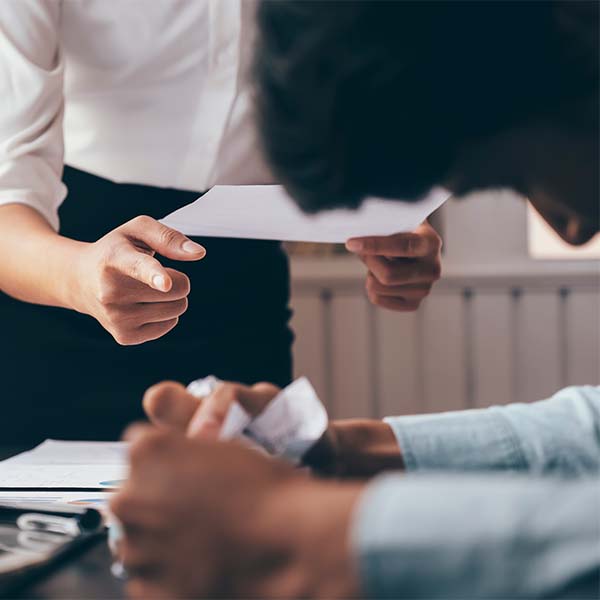 Pessoa a apontar para um documento, enquanto outra está sentada, ilustrando um processo disciplinar no trabalho