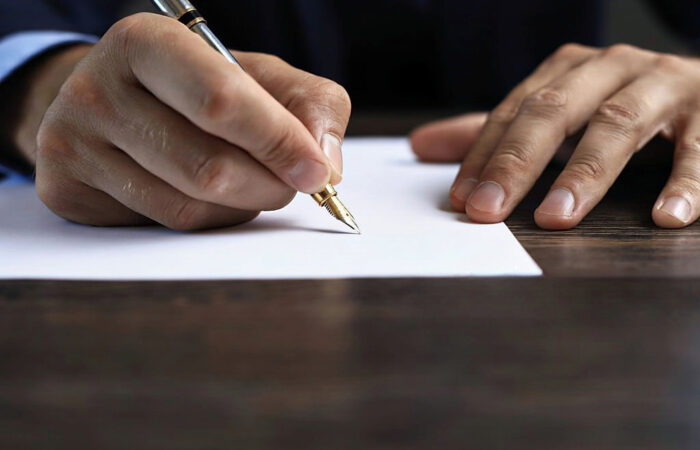 Mao direita a segurar uma caneta enquanto assina a rescisão do contrato de trabalho