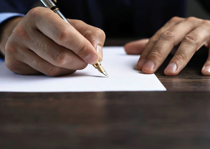 Mao direita a segurar uma caneta enquanto assina a rescisão do contrato de trabalho