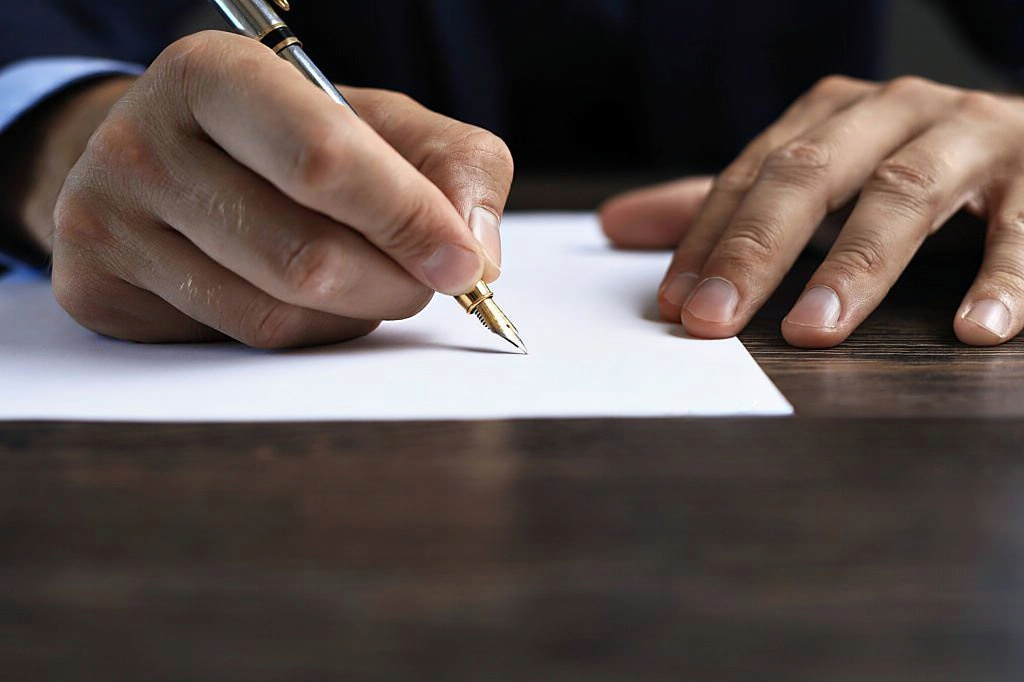 Mao direita a segurar uma caneta enquanto assina a rescisão do contrato de trabalho