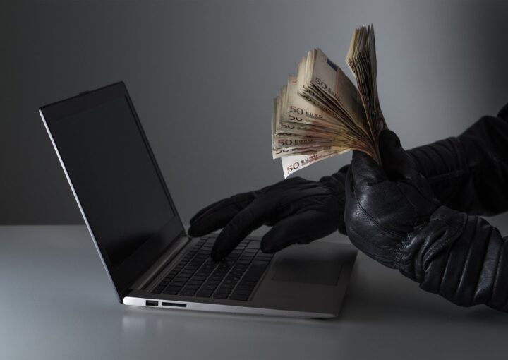 conceito de burla informatica com um criminoso com muito dinheiro na mão e a utilizar um computador portátil com luvas de cabedal pretas.