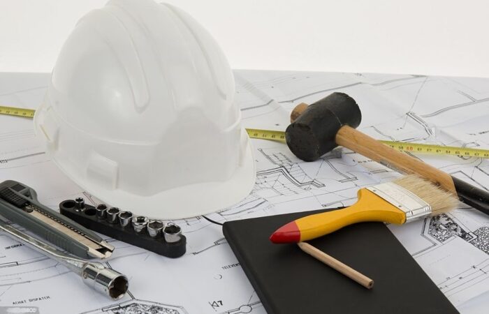 Chapeu de sefurança, martelo, pincel pousados numa planta de um casa simbolizando uma empreitada