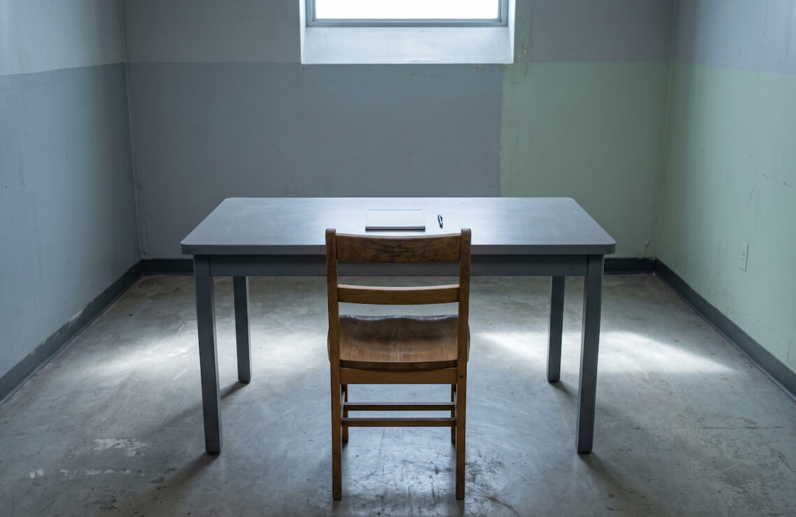 Cadeira vazia diante de uma mesa de interrogatório numa sala neutra.