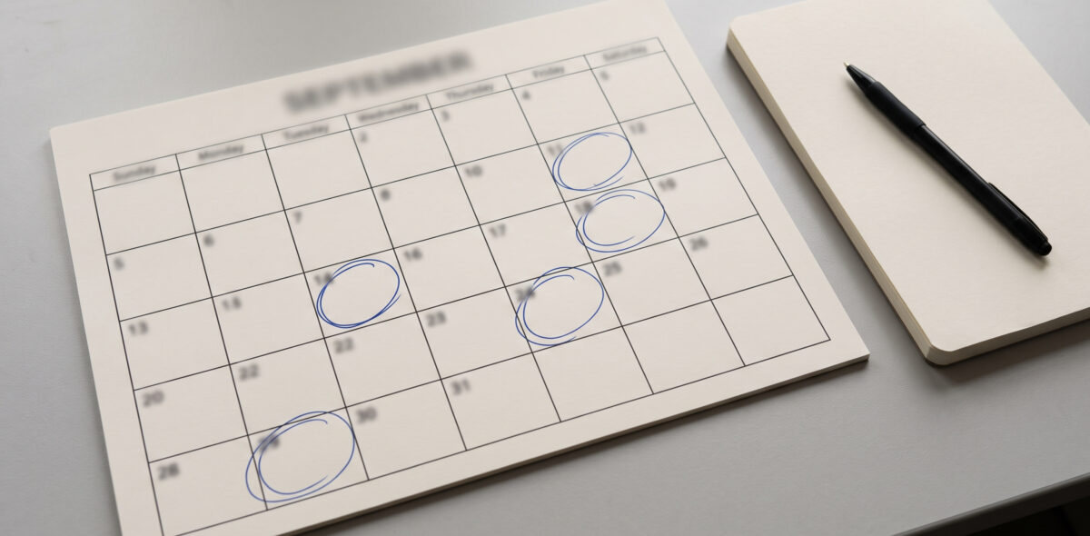 Calendário de secretária com dias assinalados a caneta ao lado de um bloco de notas