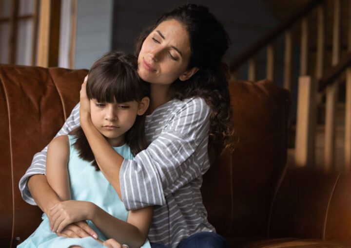 Mãe abraça a filha no sofá da sala com ausência do pai