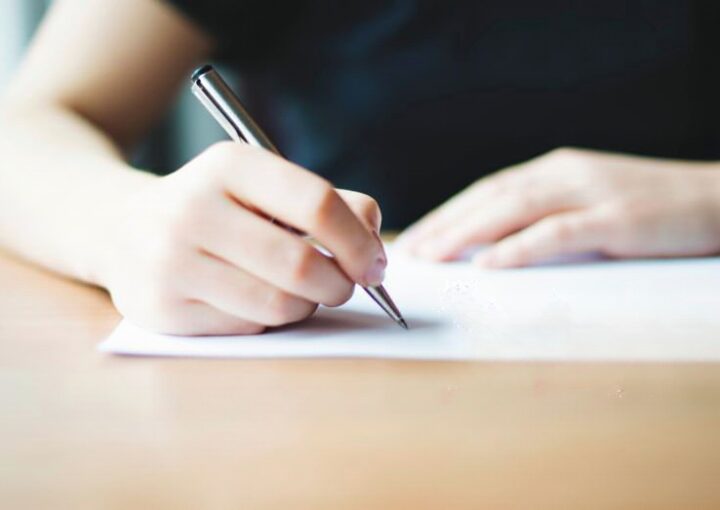 Uma pessoa sentada em frente a uma secretaria a assinar a nota de culpa com uma caneta