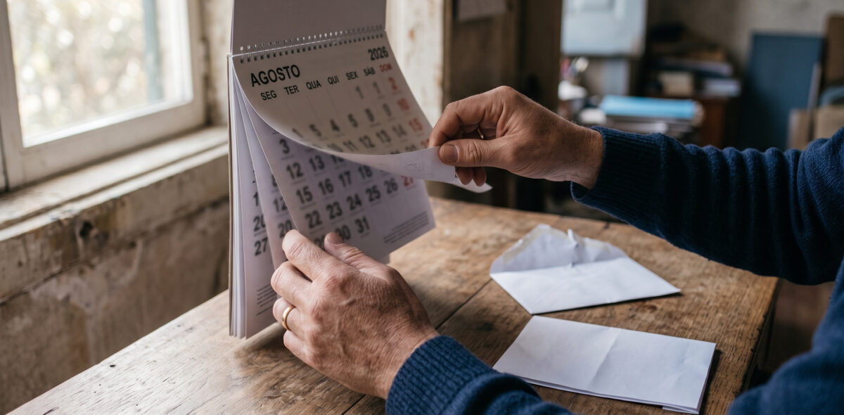 Mãos a folhear um calendário de parede junto a um envelope com correspondência da seguradora