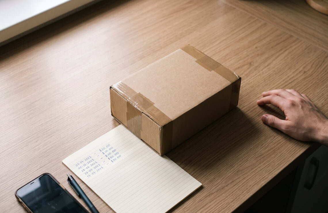 Encomenda por abrir sobre uma mesa, ao lado de uma lista de datas e valores escrita à mão.