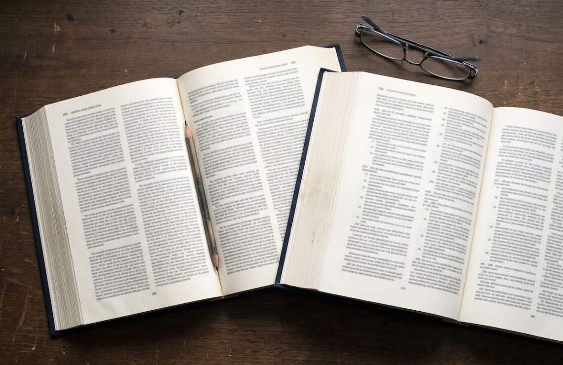 Dois códigos legais abertos lado a lado sobre a secretária, com óculos de leitura ao lado.