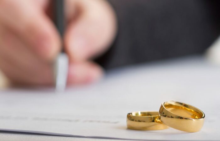 Pessoa a assinar com duas alianças em frente a simbolizar um casamento à distância