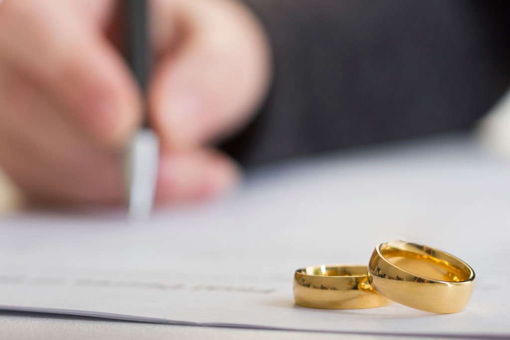 Pessoa a assinar com duas alianças em frente a simbolizar um casamento à distância
