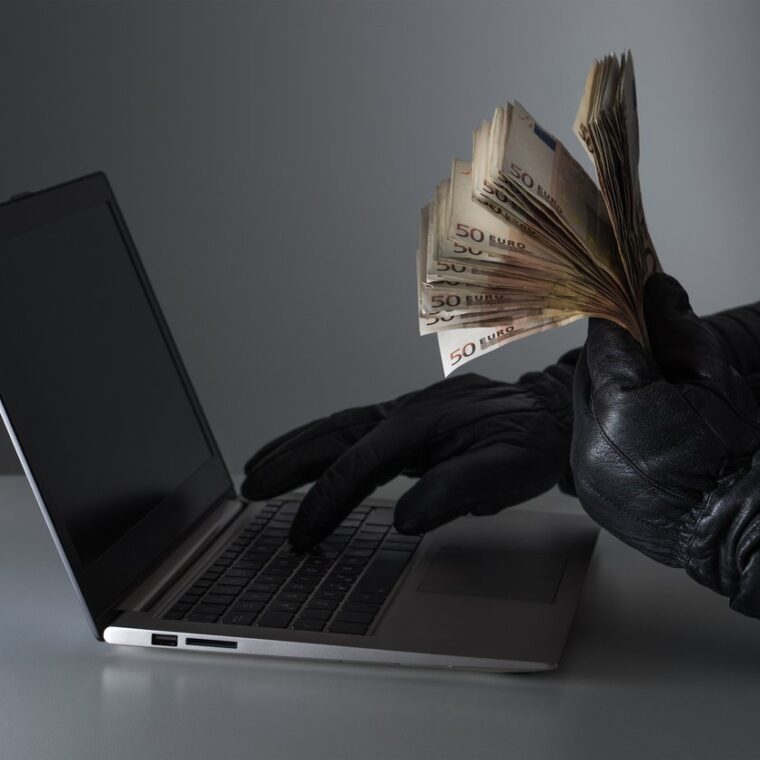 internet fraud and cyber security concept. criminal holding a lot of money and using laptop with black leather gloves.