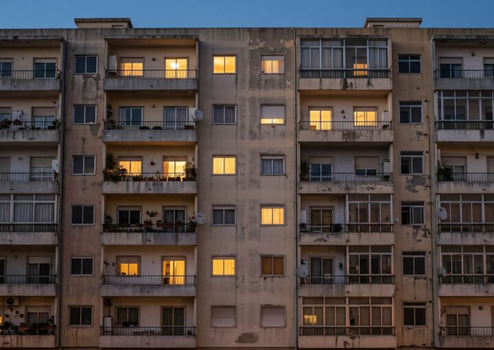 Fachada de um prédio de habitação ao anoitecer, com algumas janelas iluminadas
