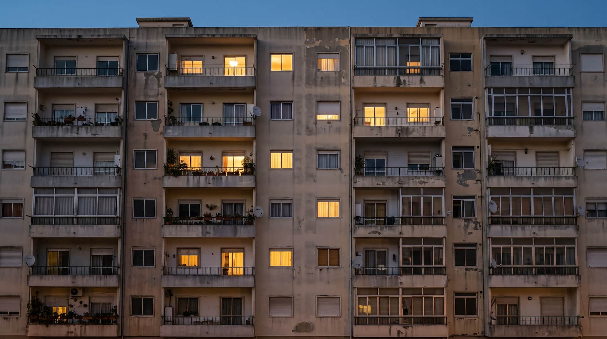 Fachada de um prédio de habitação ao anoitecer, com algumas janelas iluminadas