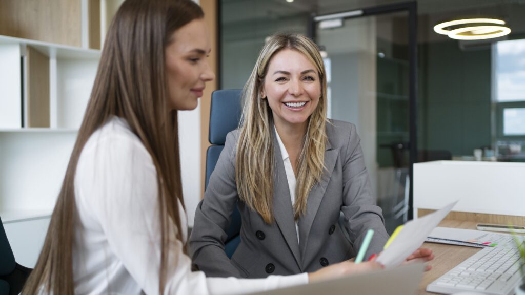 Uma advogada de família sorridente em ambiente de escritório, analisando documentos com uma cliente para um processo de casamento por procuração.