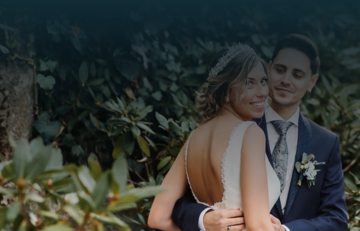 Noiva sorridente abraçada pelo noivo num ambiente de jardim, com folhagens verdes ao fundo.