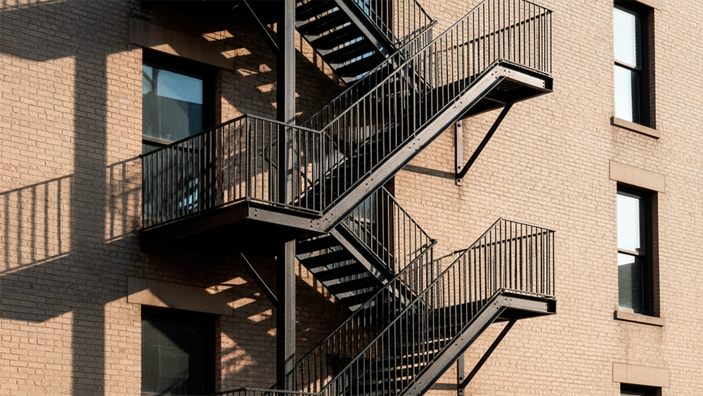 Escada metálica exterior de emergência fixada à parede de um edifício, com vários patamares visíveis.