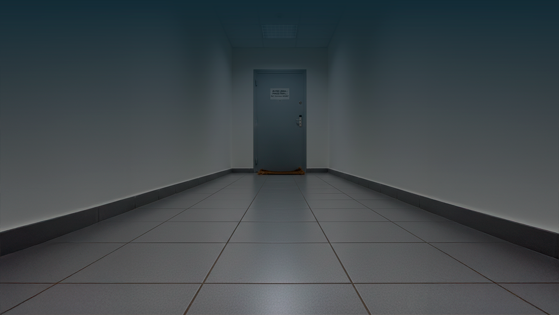 Porta de apartamento fechada num prédio residencial, com um aviso em papel afixado ao centro e um tapete gasto no chão do corredor.