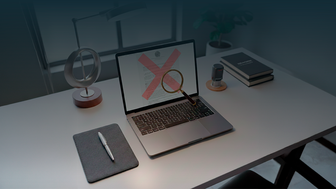 Portátil aberto exibindo edital de concurso público com um 'X' vermelho de erro e uma lupa sobre a mesa, simbolizando a análise de irregularidades em documentos oficiais.