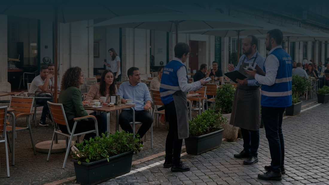 Fiscalização municipal numa esplanada movimentada em Portugal, com agentes de colete azul a falar com o gerente e clientes sentados nas mesas.