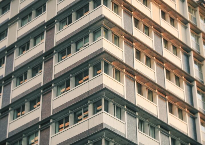 Edifício de habitação coletiva visto de baixo, com várias varandas iluminadas, refletido num espelho colocado ao nível do solo em frente à fachada.