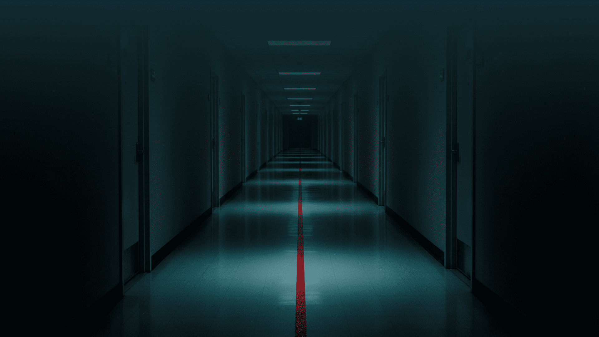 Um corredor longo e vazio, visto em perspetiva central, com portas numeradas de ambos os lados. No chão, uma única linha vermelha avança pelo corredor e desaparece ao longe. A iluminação é irregular: zonas de luz alternam com sombra, sugerindo avanço progressivo. Não há sinal de urgência imediata, apenas continuidade inevitável. Imagem de capa editorial para a pergunta: o que acontece quando nada é feito.