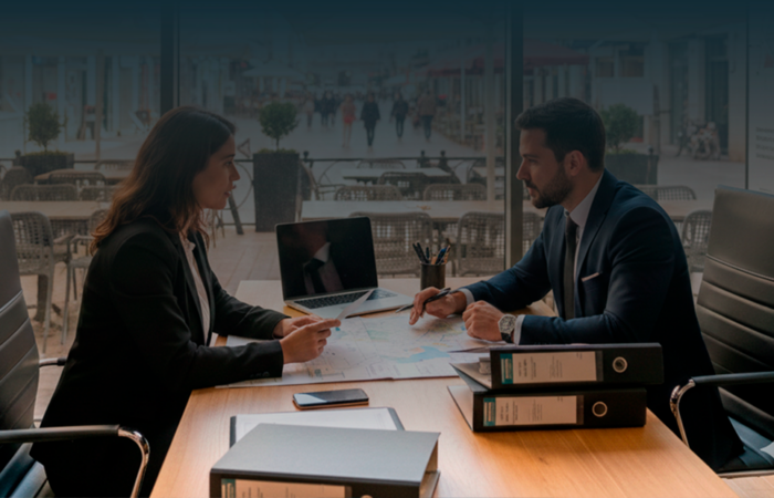 Advogados em reunião num escritório moderno com vista para uma rua de Lisboa com esplanadas e restaurantes, discutindo documentos de licenciamento público.