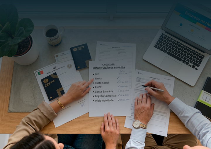 Vista superior de uma mesa de trabalho com documentos, checklist, passaporte e um portátil, ilustrando os passos e prazos para constituir uma empresa em Portugal.