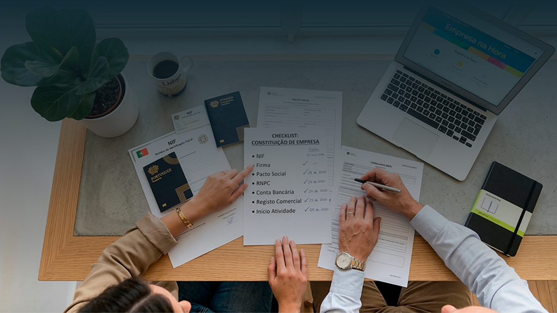 Vista superior de uma mesa de trabalho com documentos, checklist, passaporte e um portátil, ilustrando os passos e prazos para constituir uma empresa em Portugal.