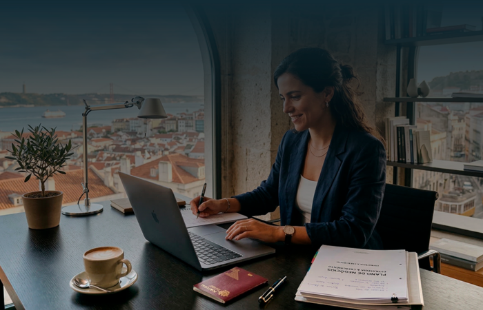 Empreendedora a trabalhar num escritório com vista para Lisboa, analisando documentos e portátil para abrir empresa em Portugal.