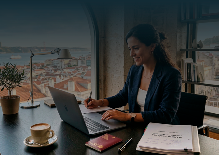 Empreendedora a trabalhar num escritório com vista para Lisboa, analisando documentos e portátil para abrir empresa em Portugal.