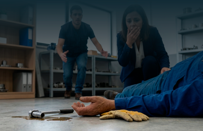 Colegas de trabalho assustados e preocupados aproximam-se de trabalhador acidentado no chão, simbolizando o momento de um acidente de trabalho.