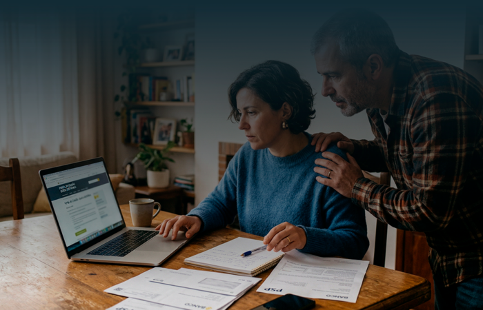 Homem preocupado sentado à mesa com computador e documentos, a receber apoio de uma mulher que lhe toca no ombro. Contexto de resolução de burla em Portugal.