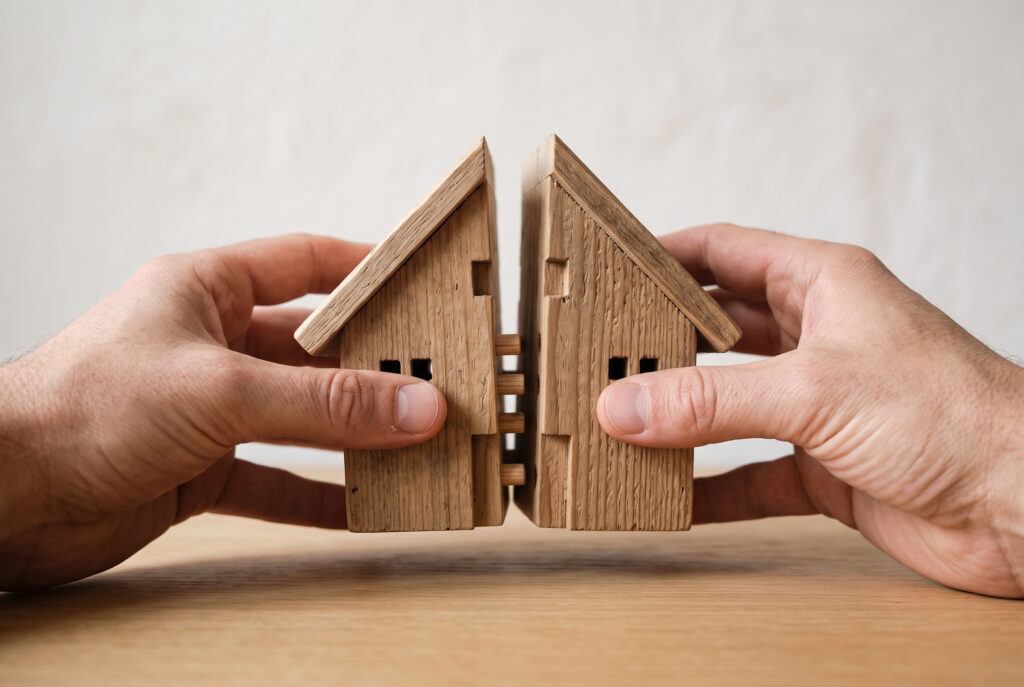 Duas metades de uma casa em miniatura a serem unidas por mãos, a simbolizar a consolidação da propriedade plena