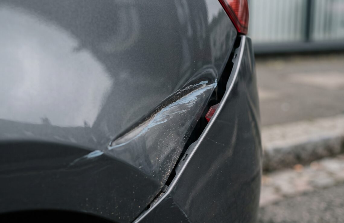 Pormenor do painel amassado de um carro com risco de tinta de outra cor, único vestígio deixado pelo veículo que fugiu.