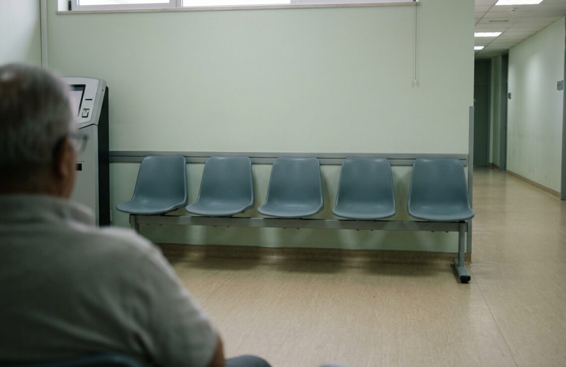 Sala de espera de um serviço público com cadeiras vazias e um distribuidor de senhas.