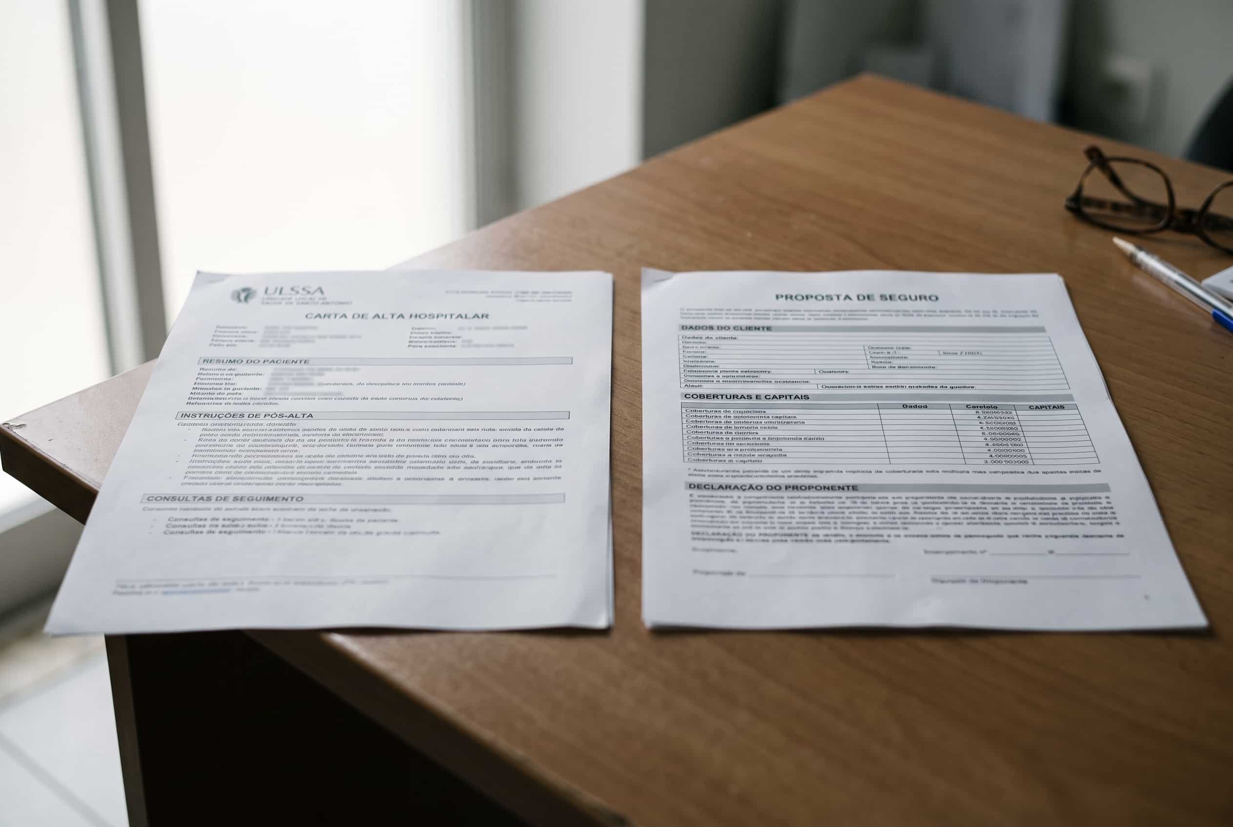 Carta de alta médica e proposta de seguro de vida pousadas lado a lado sobre uma mesa.