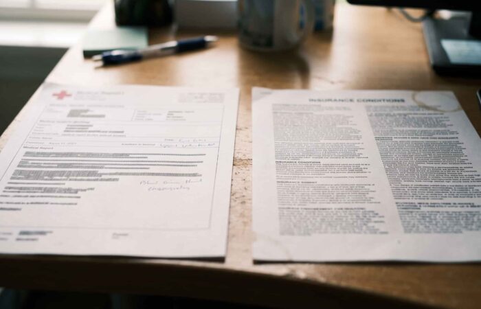 Relatório médico e condições de uma apólice de seguro de vida lado a lado sobre uma mesa de escritório.