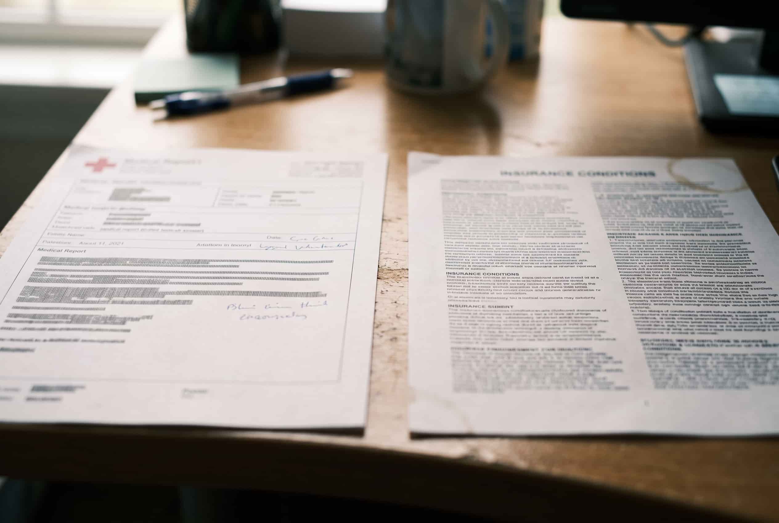 Relatório médico e condições de uma apólice de seguro de vida lado a lado sobre uma mesa de escritório.