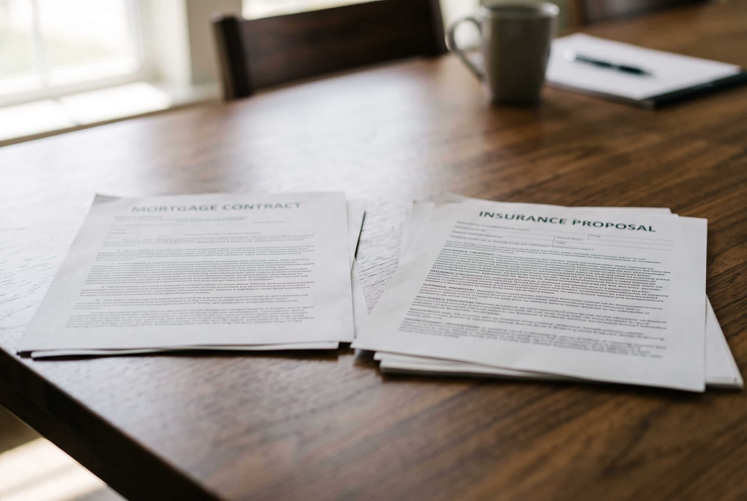 Contrato de crédito à habitação e proposta de seguro de vida sobre uma mesa de reunião.