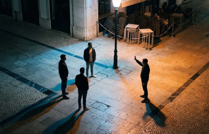 Três homens juntos à porta de um bar à noite, virados para uma quarta pessoa fora do enquadramento.