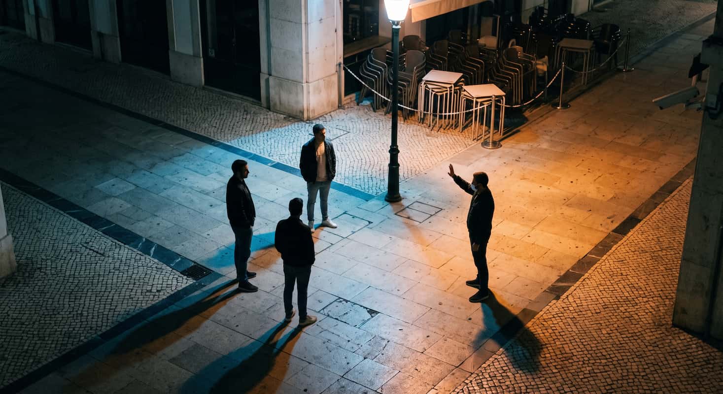 Três homens juntos à porta de um bar à noite, virados para uma quarta pessoa fora do enquadramento.