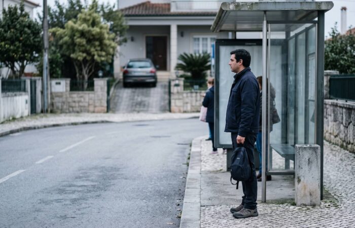 Homem à espera do autocarro com o carro estacionado atrás