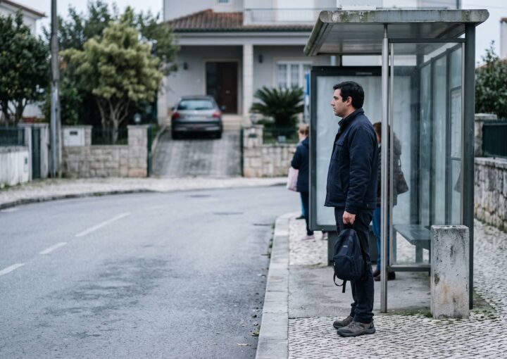 Homem à espera do autocarro com o carro estacionado atrás