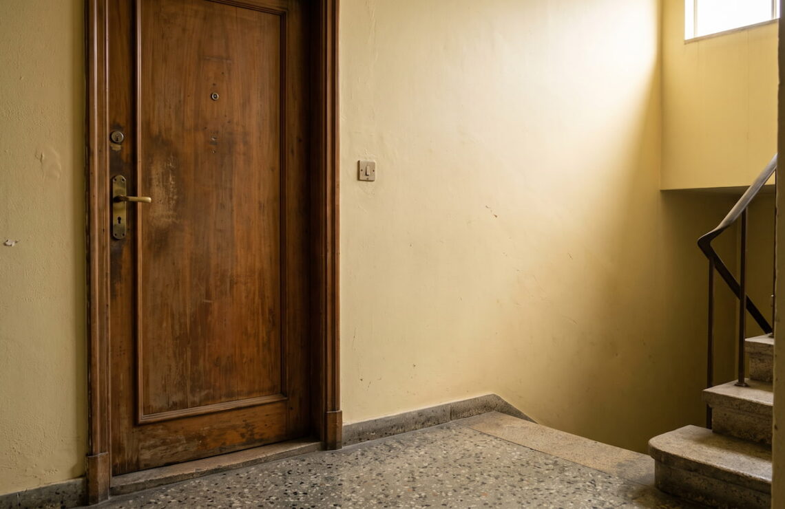 Porta fechada de um apartamento num patamar de prédio antigo, ao fim da tarde